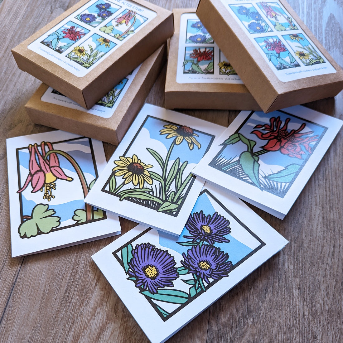 A stack of boxes of wildflower stationery sets that include cards with pictures of wild columbine, New England asters, black-eyed Susans, and scarlet bee balm flowers on them.