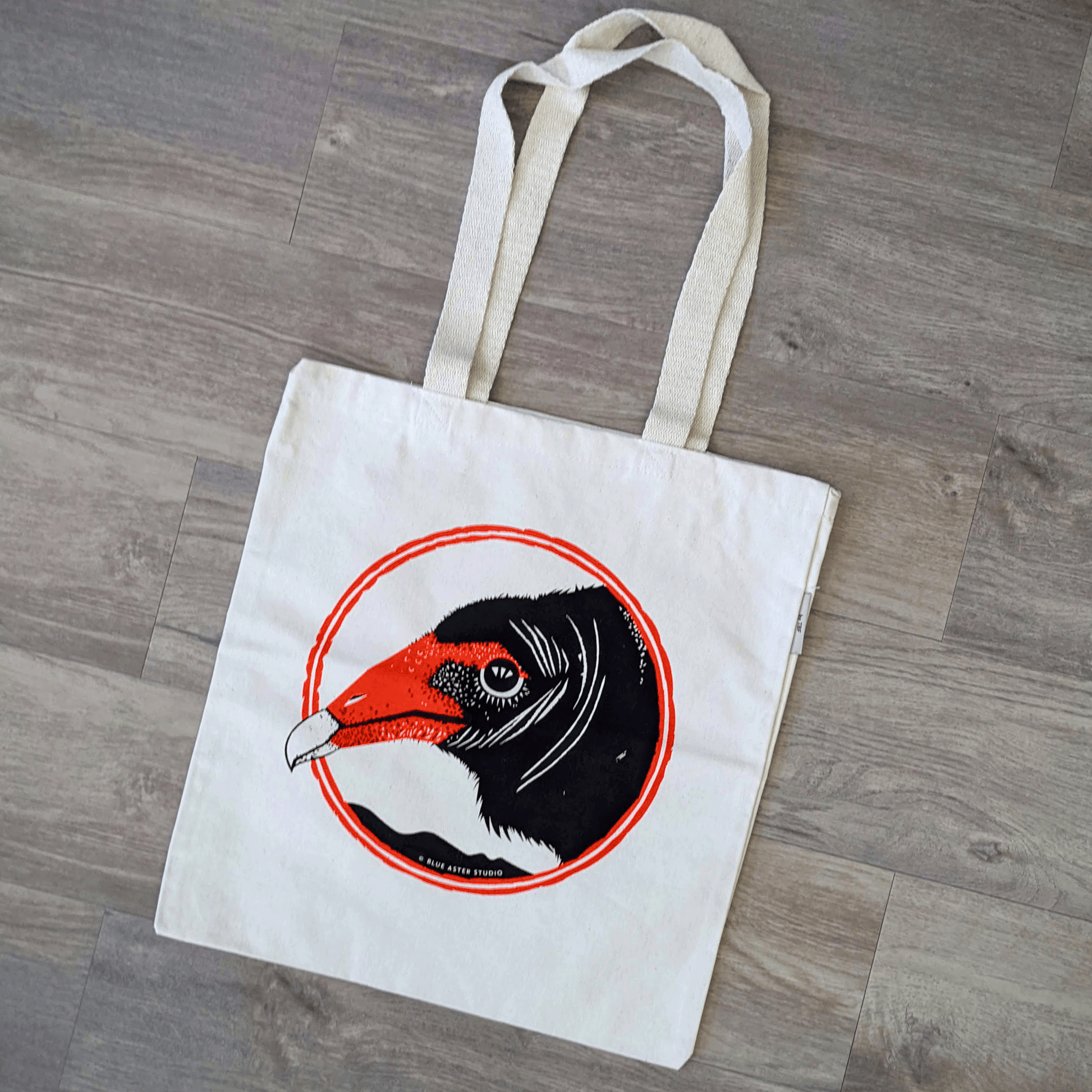 An organic cotton turkey vulture tote bag. The bag has a turkey vulture face screen printed on it in black and red.