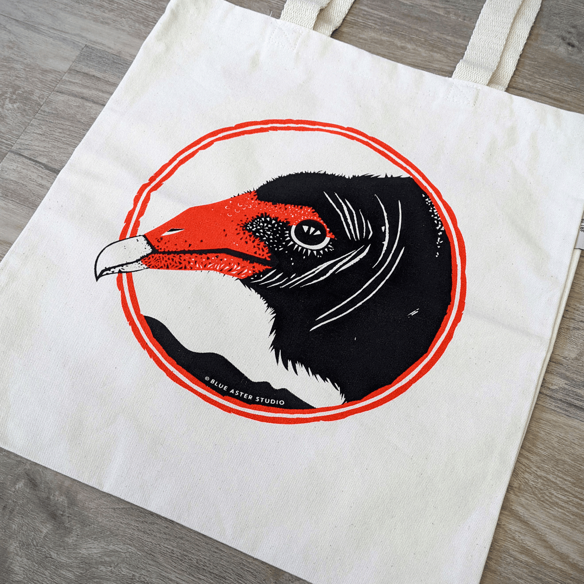 An organic cotton turkey vulture tote bag. The bag has a turkey vulture face screen printed on it in black and red.