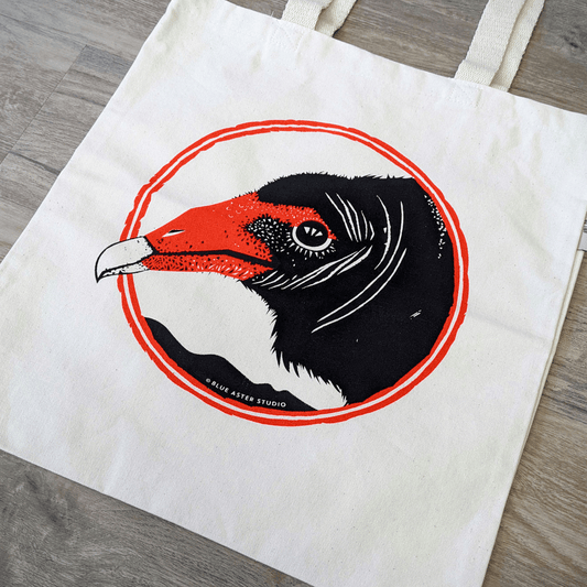 An organic cotton turkey vulture tote bag. The bag has a turkey vulture face screen printed on it in black and red.