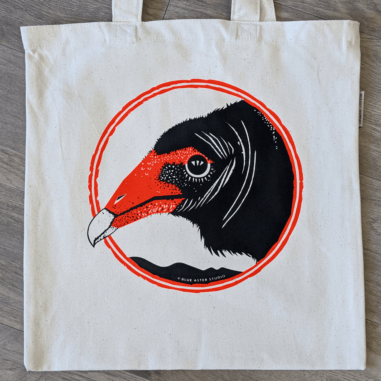 An organic cotton turkey vulture tote bag. The bag has a turkey vulture face screen printed on it in black and red.