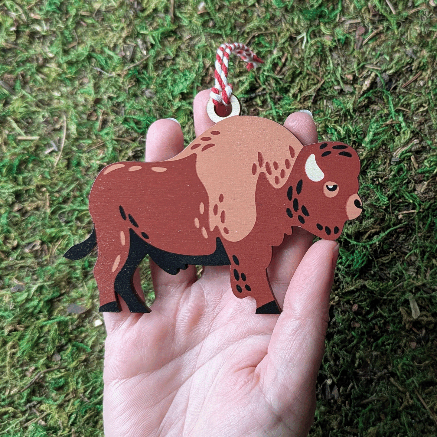 A wooden screen printed ornament of a bison held in hand.