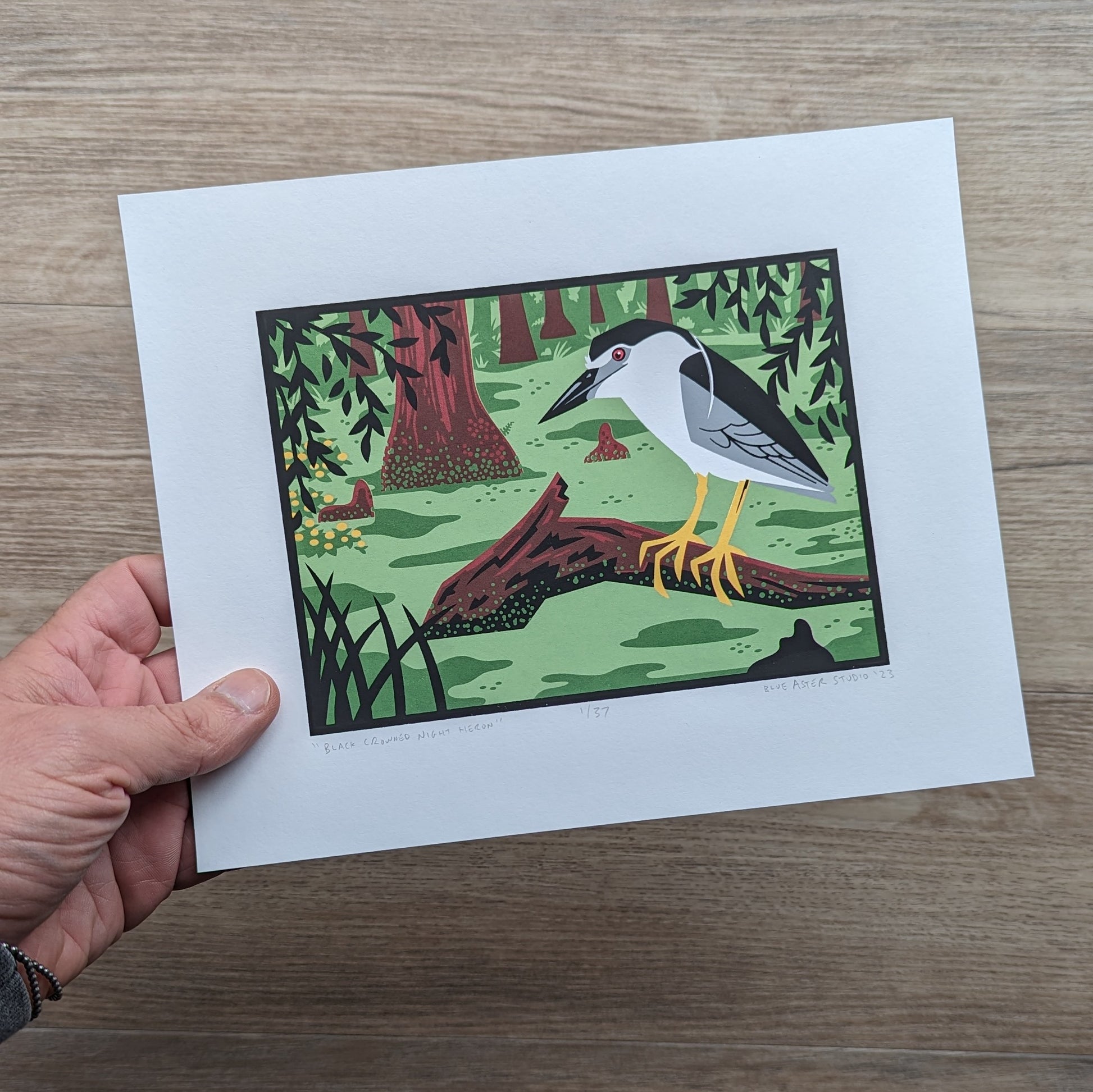 A hand holding the black crowned night heron screen print to show scale.