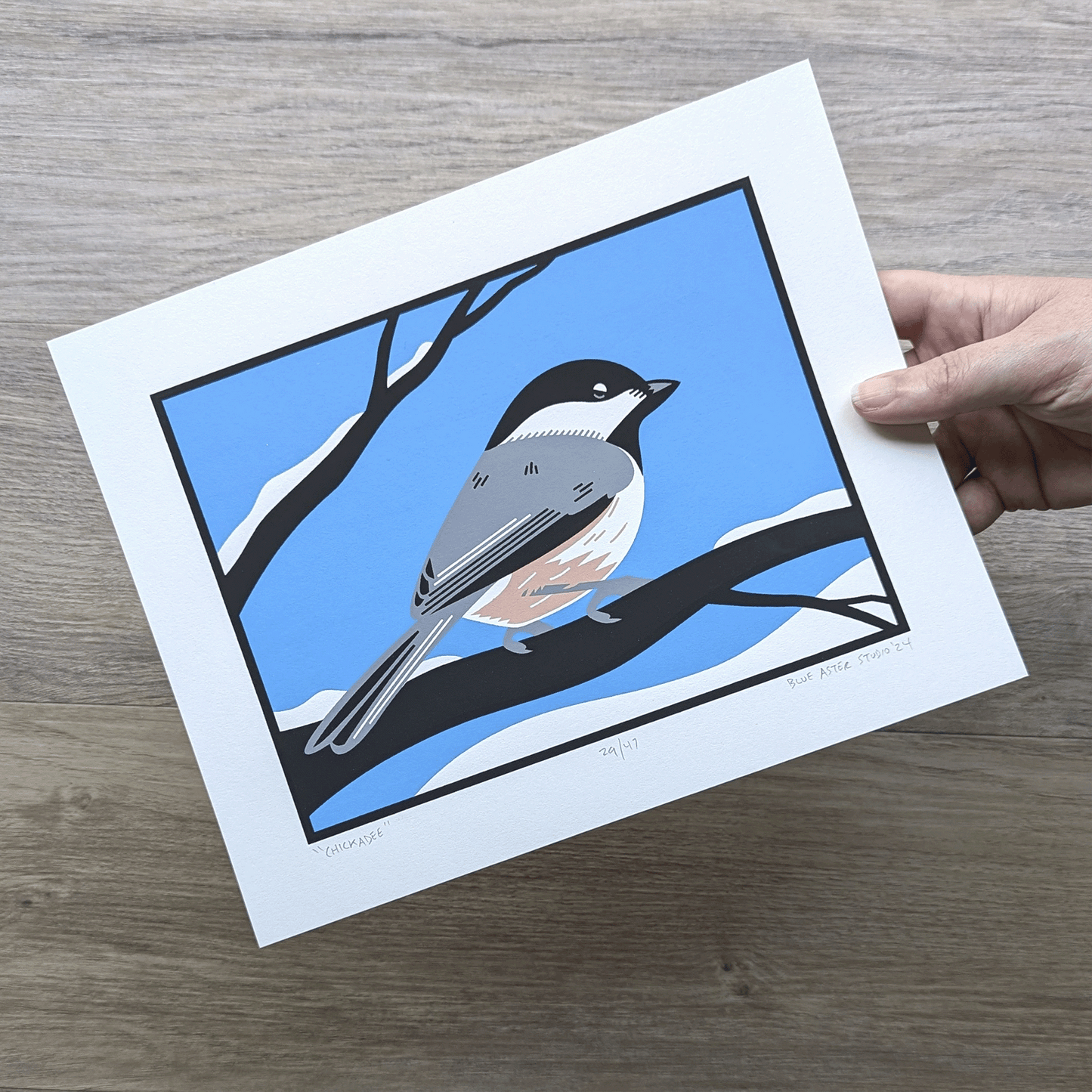 A hand holding the screen printed chickadee artwork to show scale.
