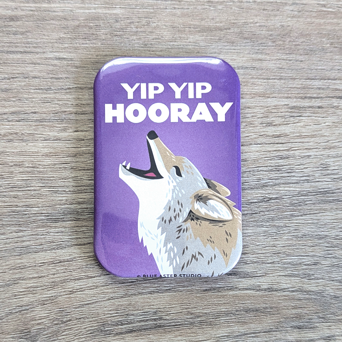 A rounded rectangle magnet of a coyote happily calling to the sky, with the text Yip Yip Hooray above it.