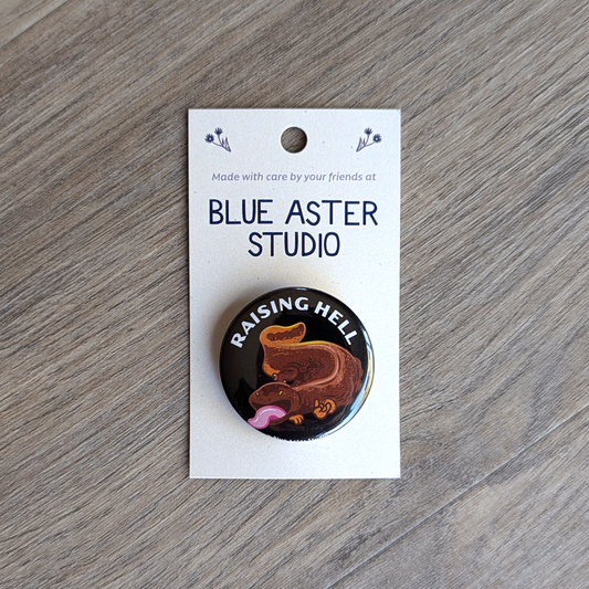 A 1.5 inch button of a hellbender with the text "raising hell."