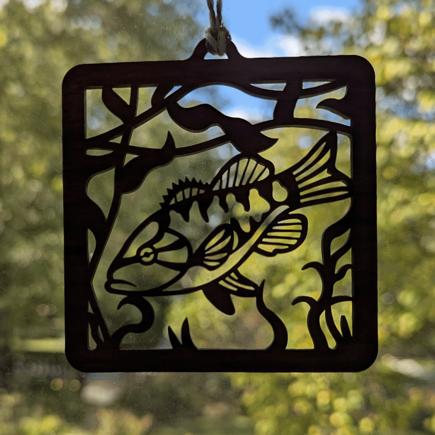 A square wooden ornament of a smallmouth bass in front of a window.