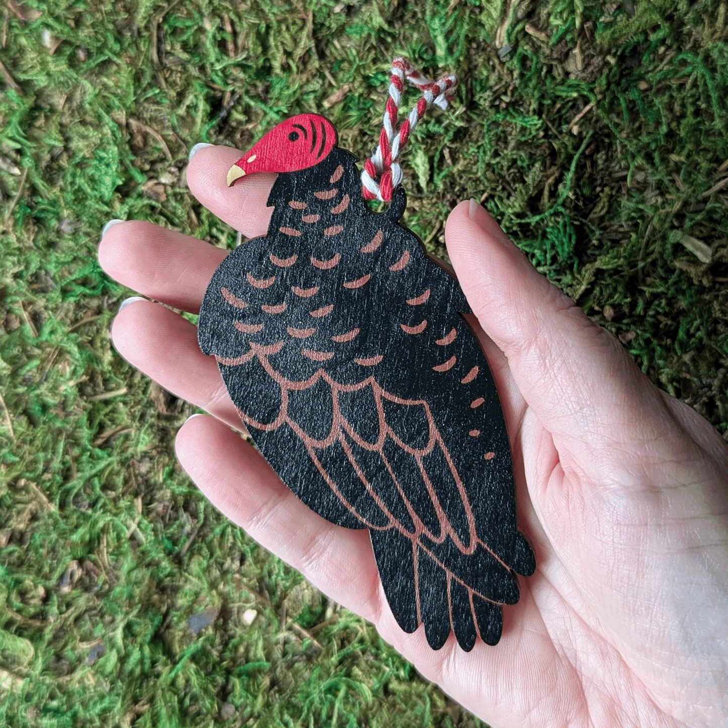 A wooden screen printed ornament of a turkey vulture held in hand.