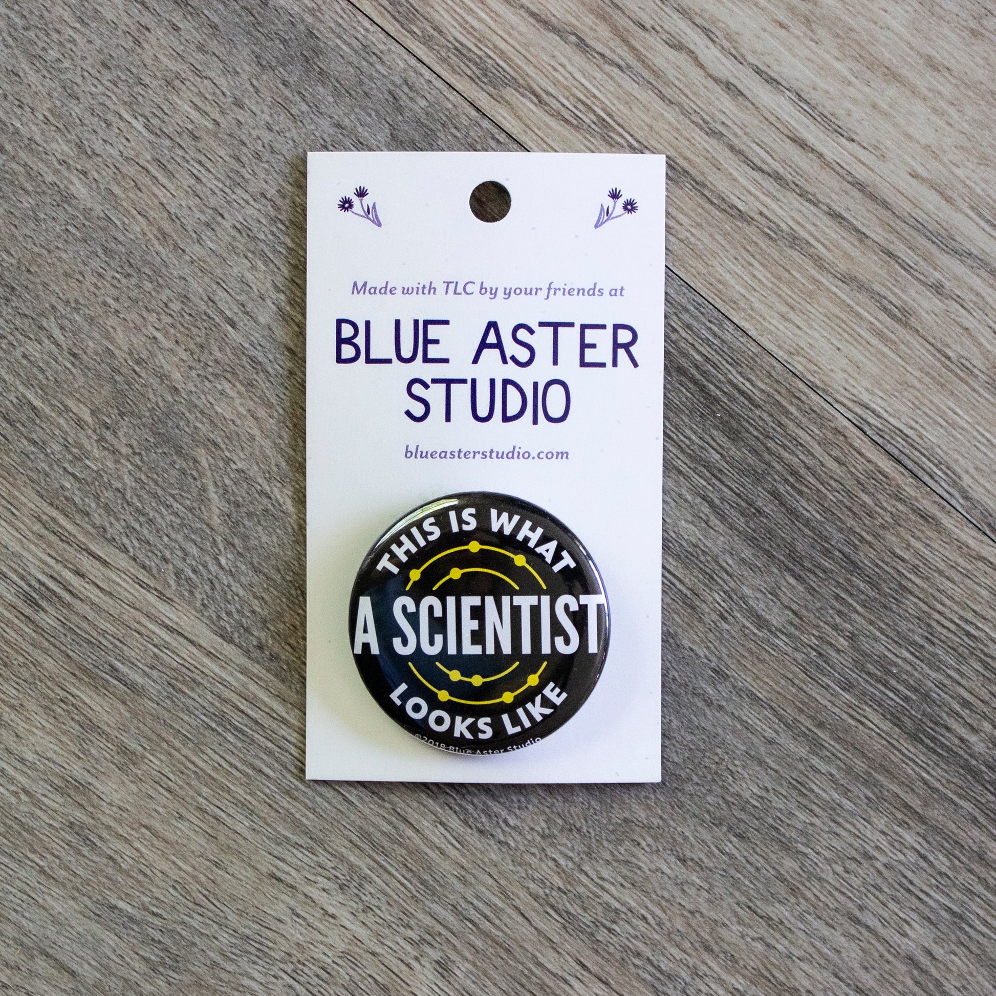 A 1.5 inch black pinback button with the words This Is What A Scientist Looks Like in white.