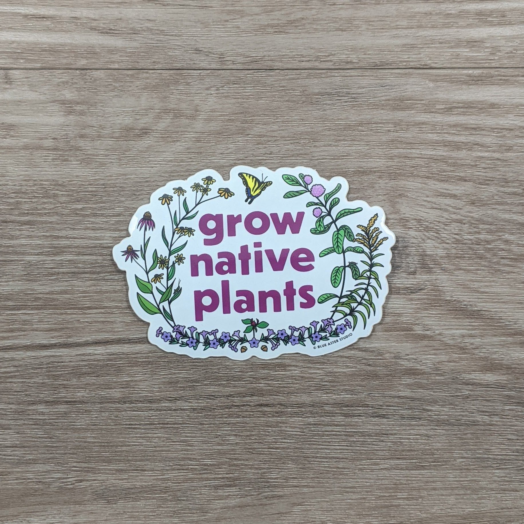 A vinyl sticker with the words Grow Native Plants surrounded by native plants including purple coneflowers, brown-eyed susans, common milkweed, goldenrod, wild petunia, and a trillium flower