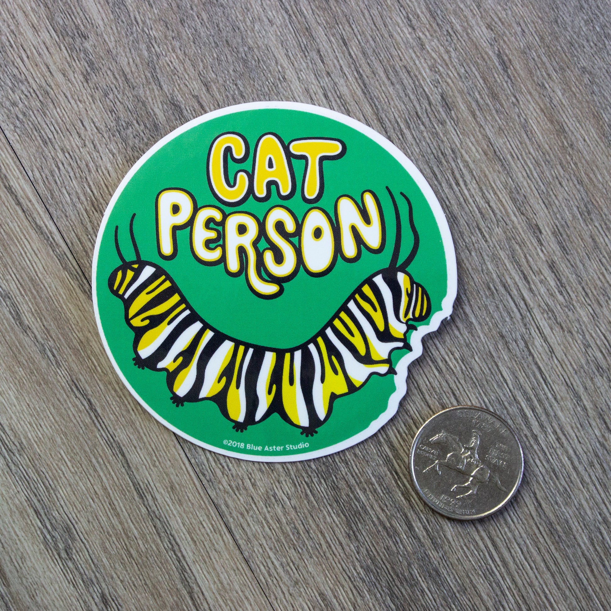 A round vinyl sticker with an illustration of a monarch caterpillar and the words Cat Person above it. A US quarter is provided for scale.