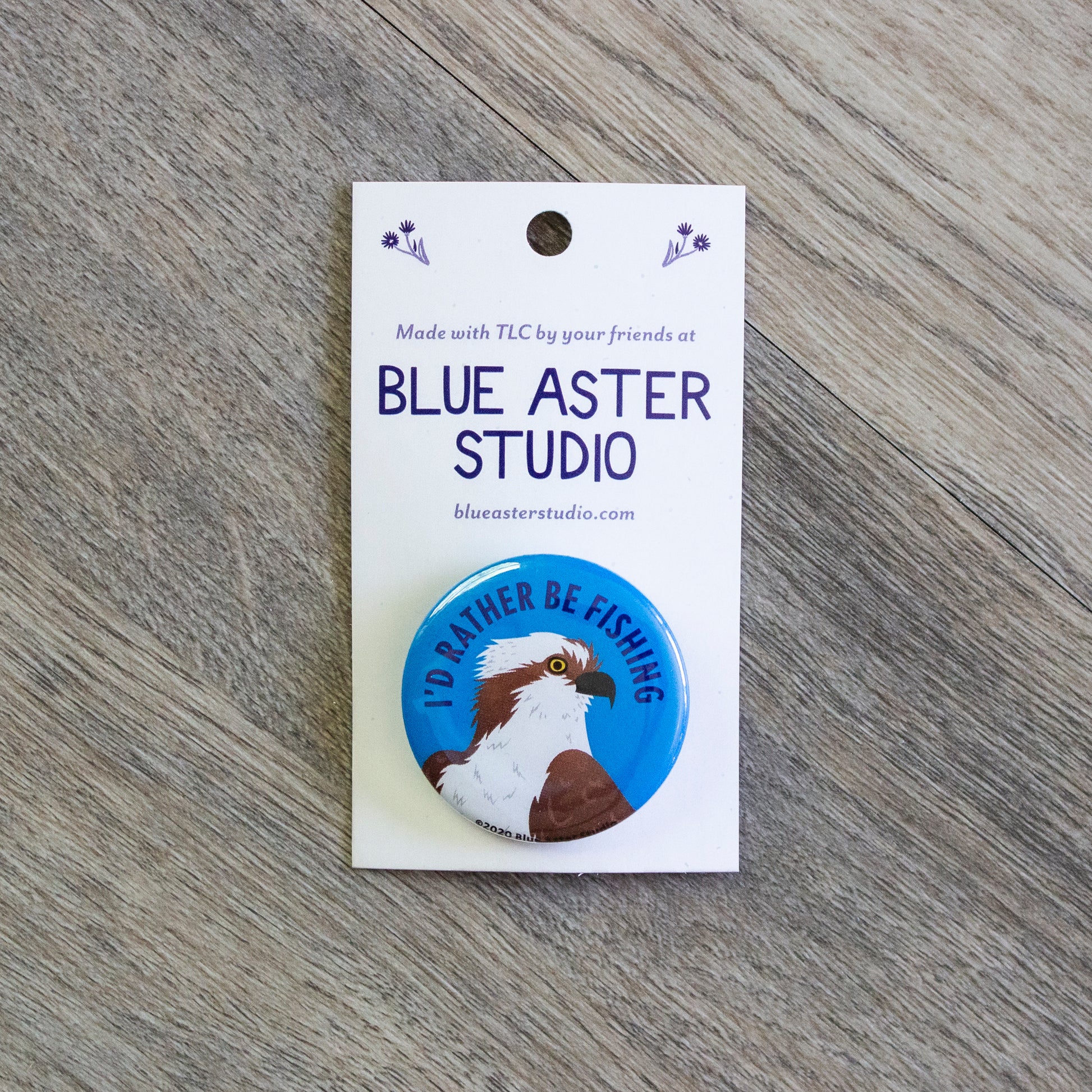 A pinback button with an illustration of an osprey and the words "I'd Rather Be Fishing"