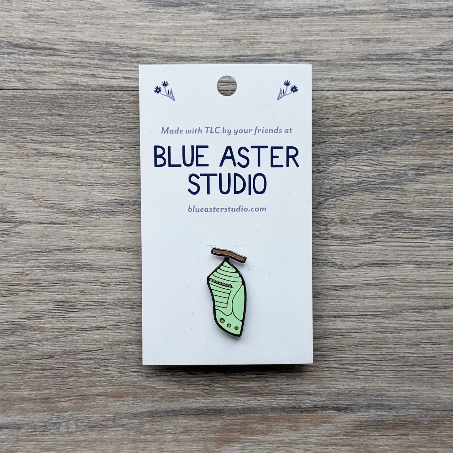 A monarch chrysalis enamel pin.