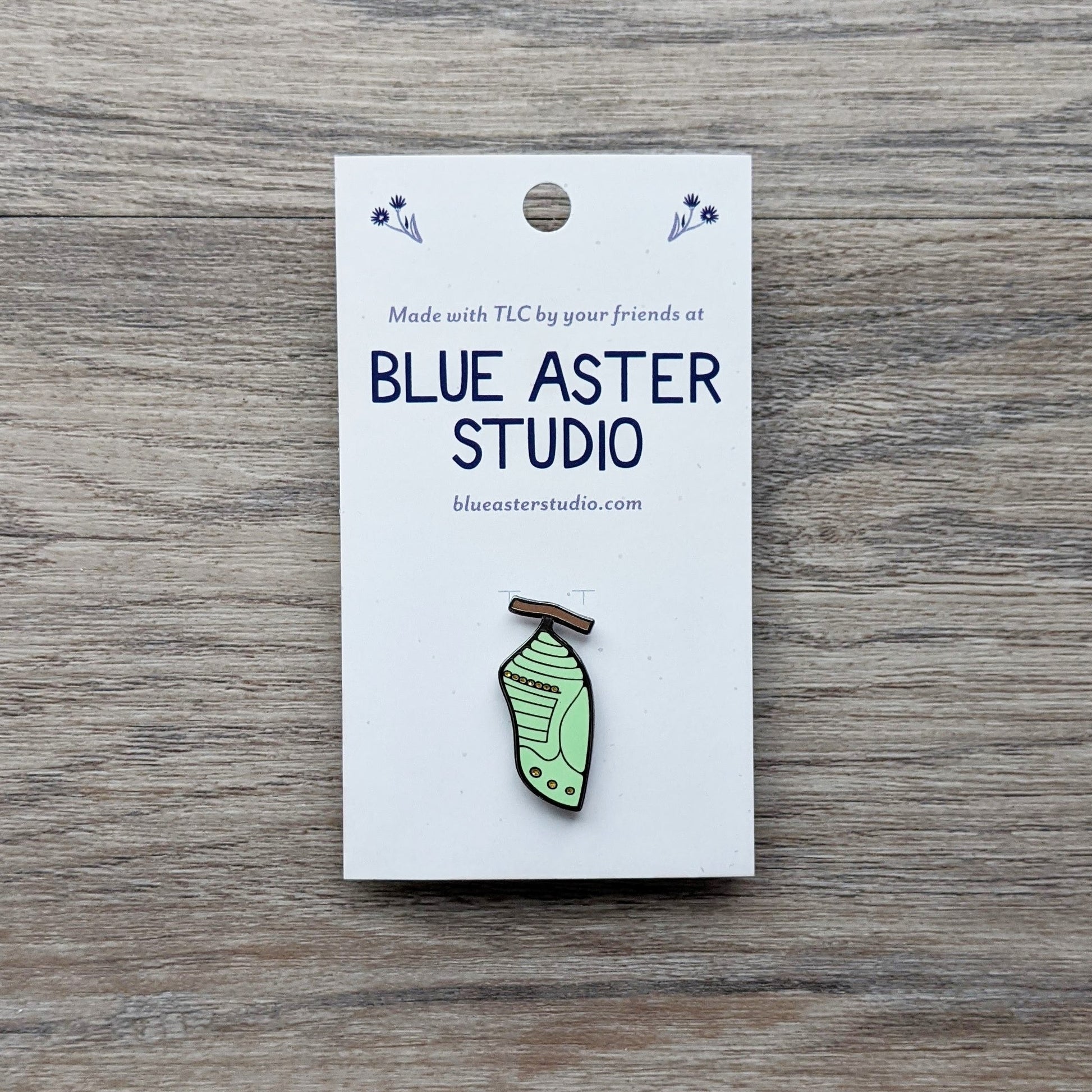 A monarch chrysalis enamel pin.