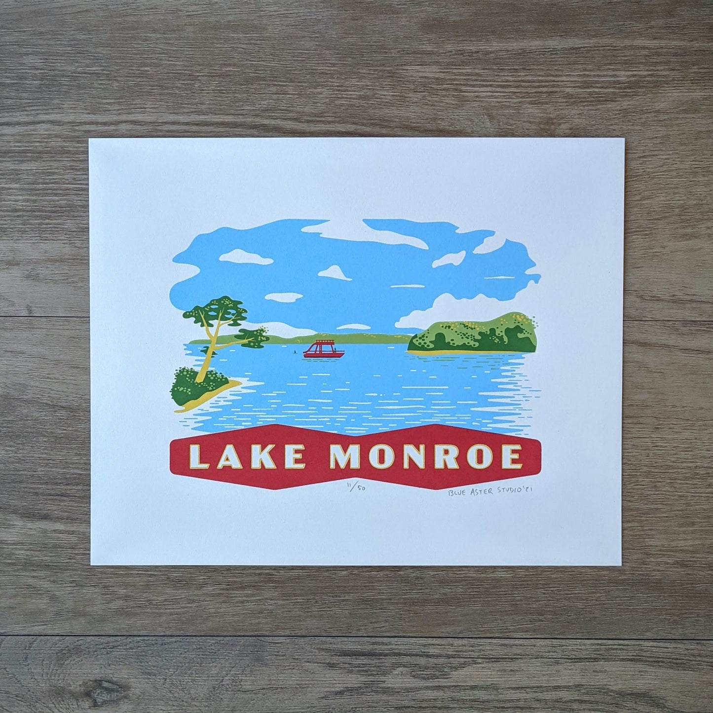 A scene on Lake Monroe that shows a pontoon boat and some swimmers surrouned by the treen lined shore of the Southern Indiana lake. At the bottom is a banner that reads "Lake Monroe." The screen print is inspired by vintage postcard art.