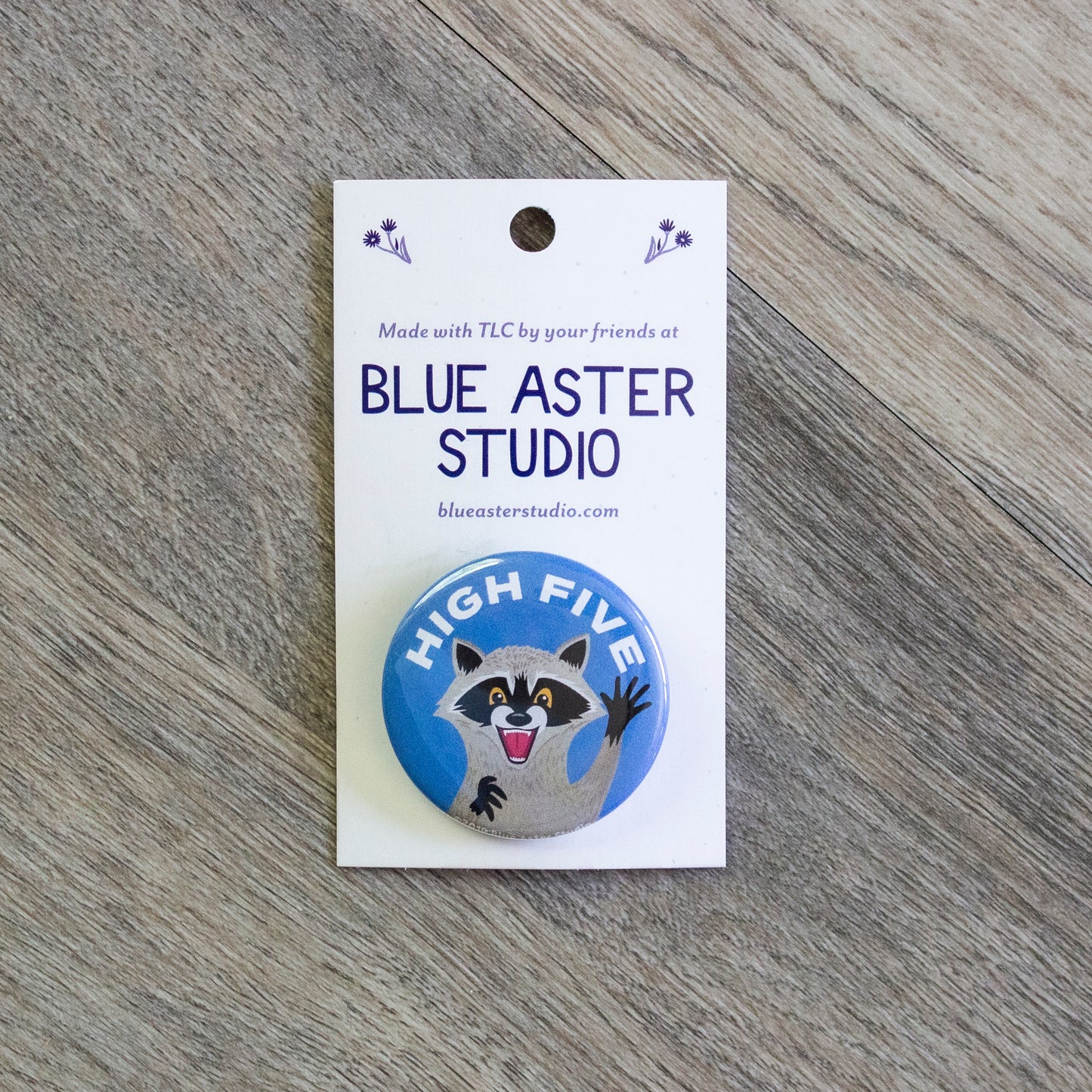 A pinback button with an illustration of a happy raccoon with its hand up with the words "High Five" above it.