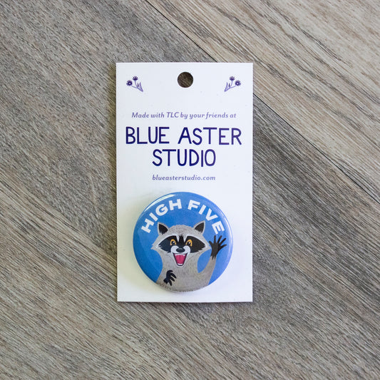 A pinback button with an illustration of a happy raccoon with its hand up with the words "High Five" above it.