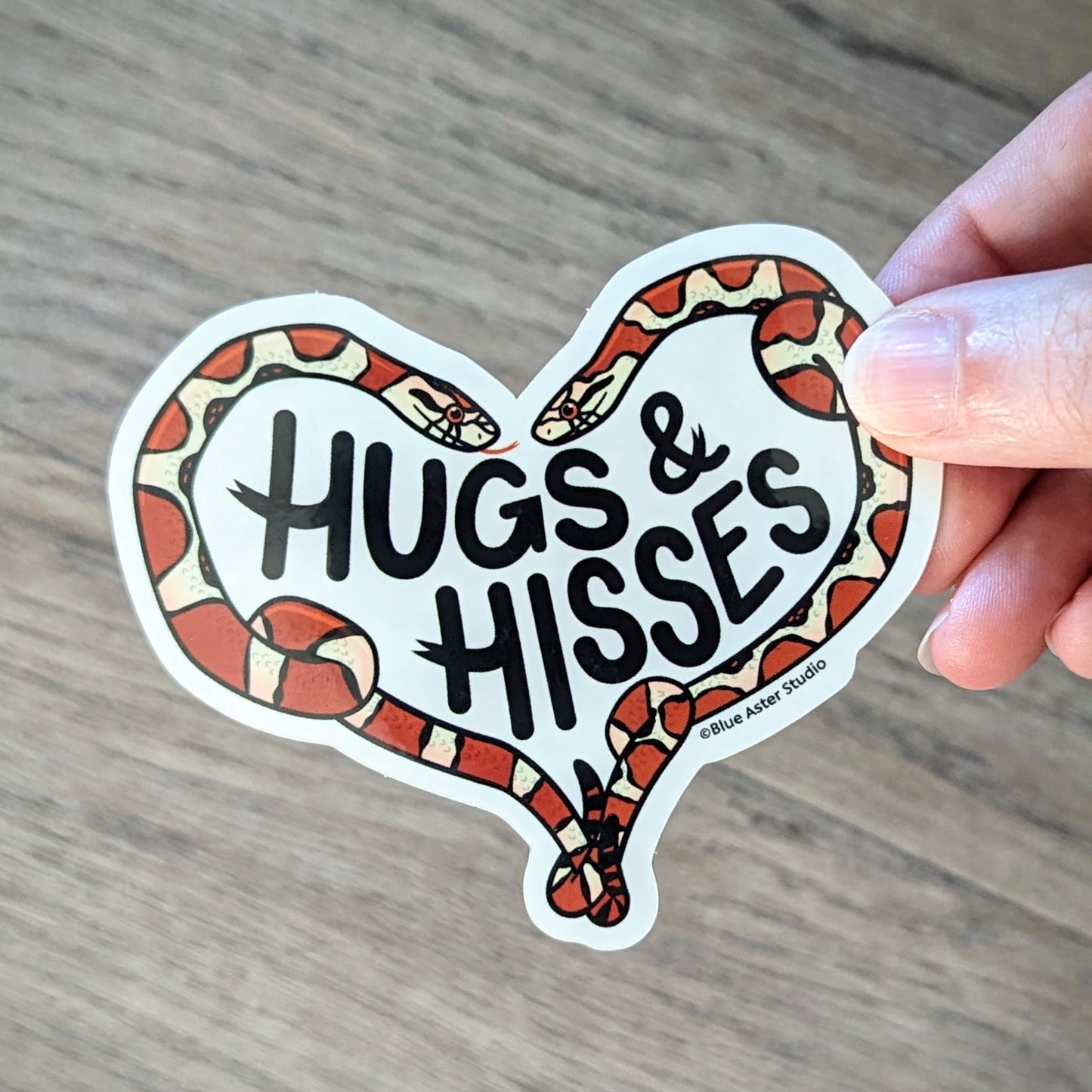 A hand holding the heartshaped snake sticker to show the scale of the design.