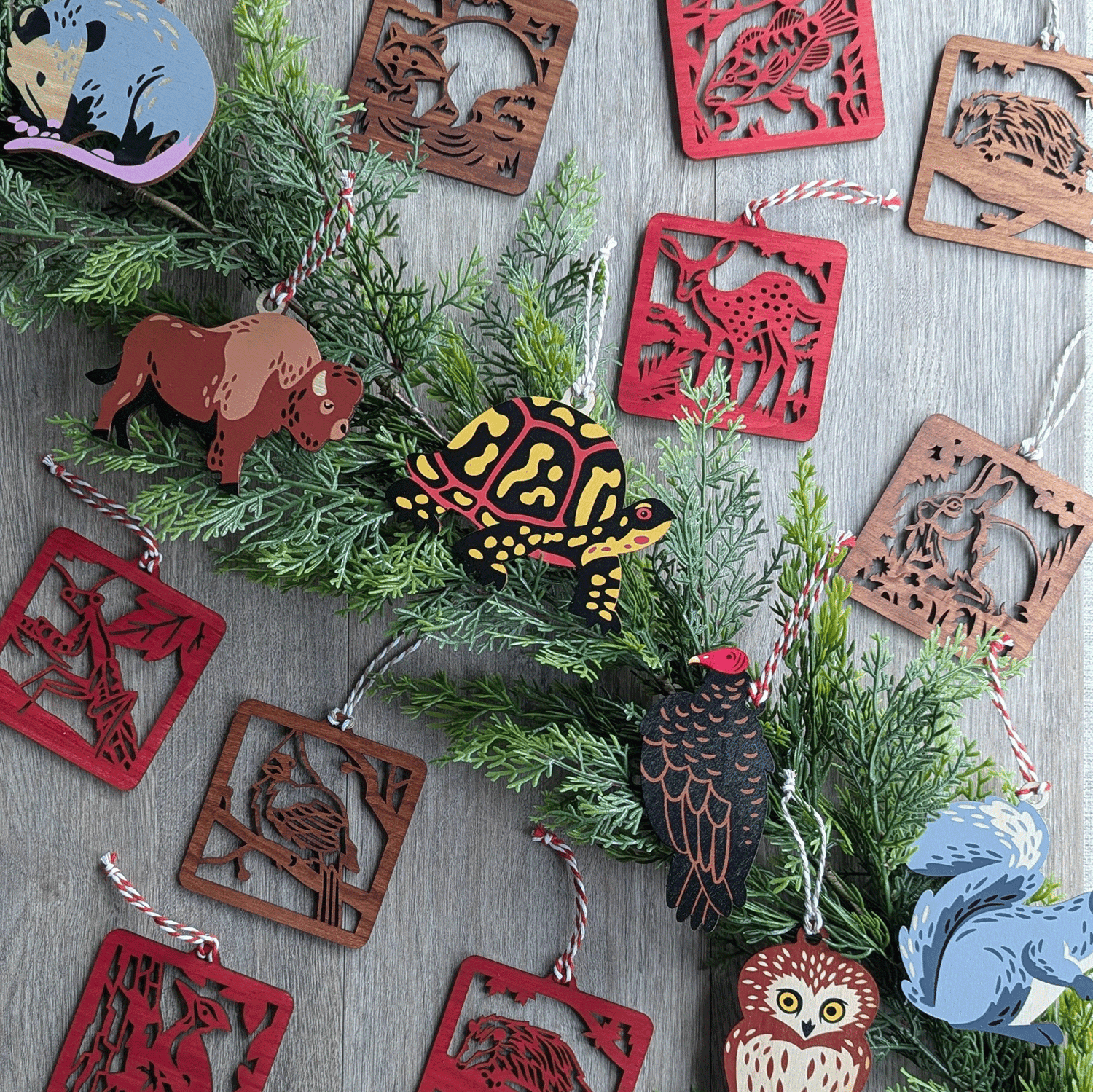 A collection of wooden wildlife ornaments arranged around a green garland. The animal designs include native fauna such as bison, opossum, box turtle, owl, cardinal, mantis, rabbit, squirrel, and turkey vulture..