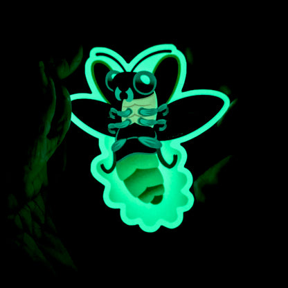 An illustrated sticker of a firefly in flights with a glowing abdomen, held in hand in the dark to show the brilliant green glow of the sticker