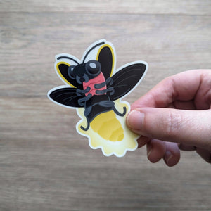 A hand holding the glow in the dark lightning bug sticker.
