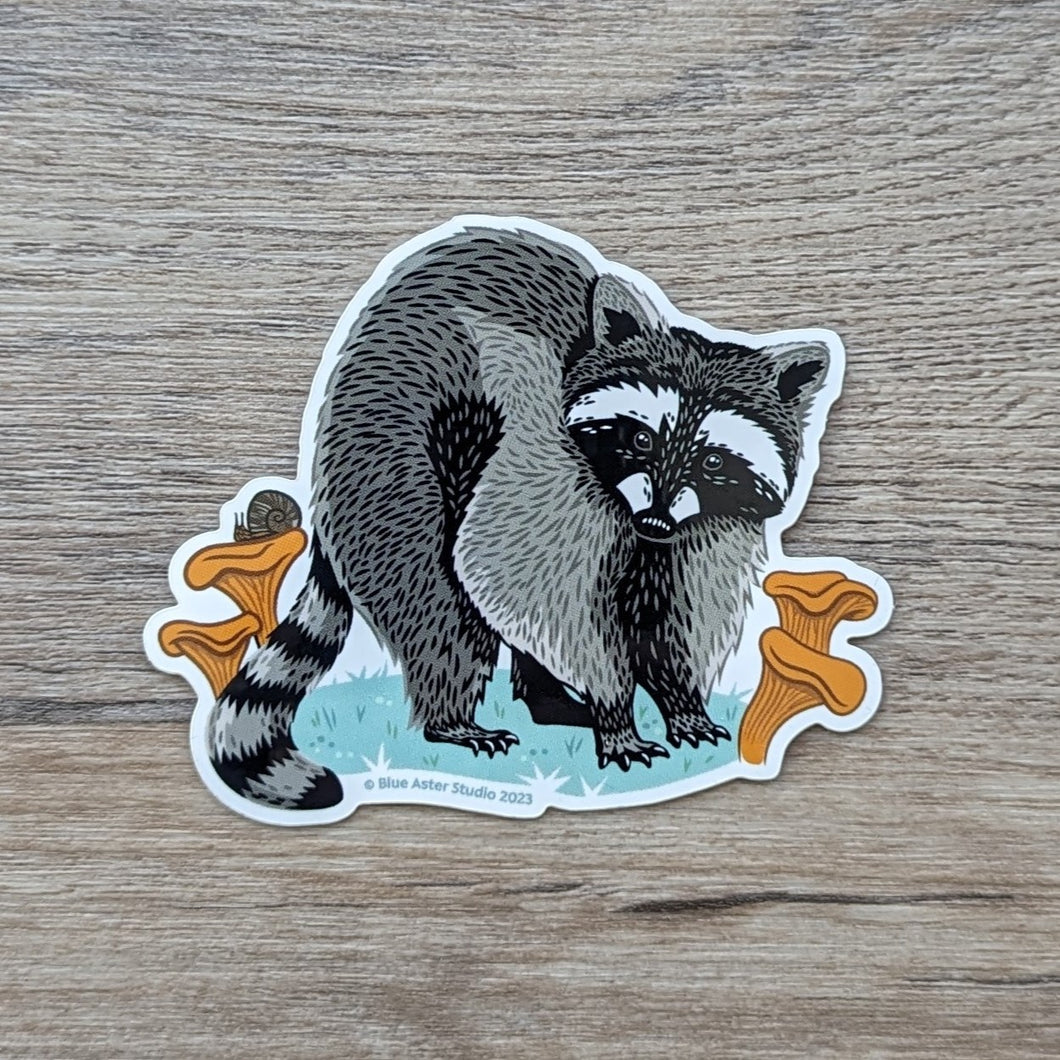 A vinyl sticker of an illustration of a raccoon surrounded by mushrooms.
