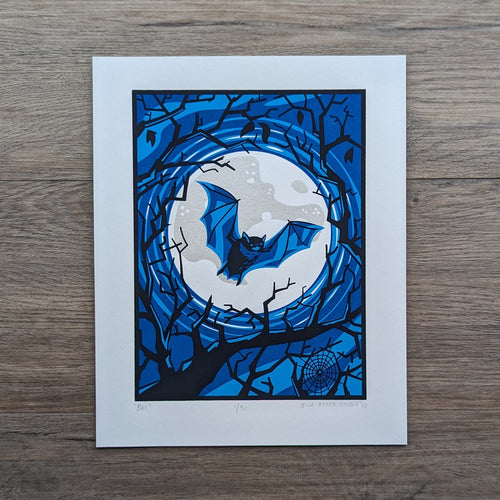 A screen print of a bat flying in front of a full moon surrounded by bare tree branch silhouettes. The print is made with four colors including two shades of blue, silver, and black.