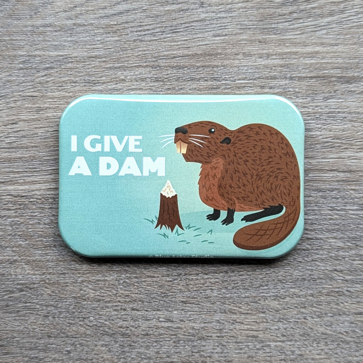 A 2 inch by 3 inch refrigerator magnet featuring an illustration of a beaver next to a tree stump that has been chewed on with the words I Give A Dam next to it.