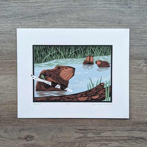 An original screen print of three beavers in a wetland setting. There is a beaver in the foreground holding a branch while two small beavers are sitting together in the background near some tall grasses.