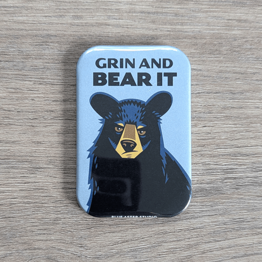 A rounded rectangular magnet with an illustrated portrait of a black bear with the text Grin and Bear It above its head.