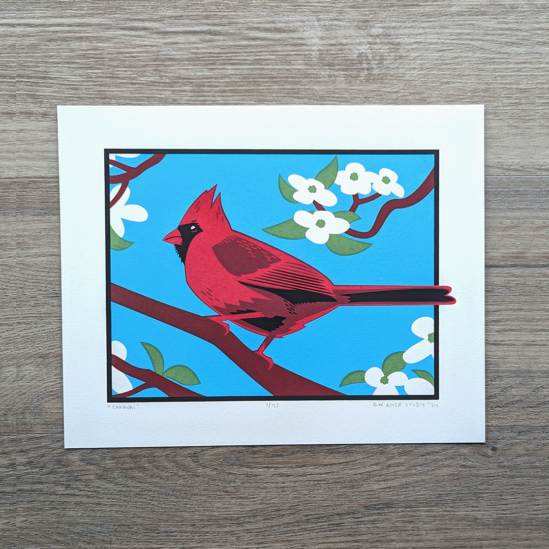 An 8x10 screen print of an illustration of a cardinal perched in a dogwood tree surrounded by white dogwood flowers against a bright blue sky.