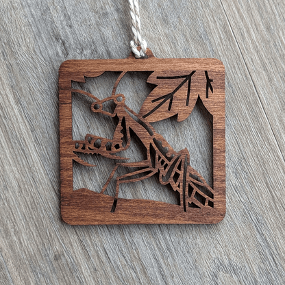 A square brown wooden ornament of a Carolina mantis.