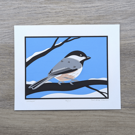 An original screen print of an illustration of a chickadee sitting on snowcovered tree branches.