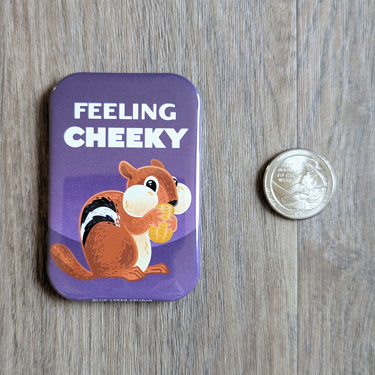 A rectangular three inch by two inch magnet featuring an illustrated chipmunk holding a peanut, set against a purple background. The text reads "Feeling Cheeky". A quarter is shown for scale.