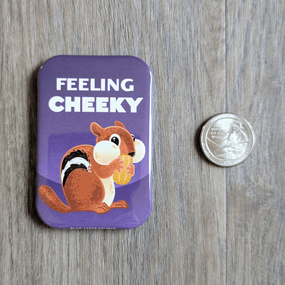 A rectangular three inch by two inch magnet featuring an illustrated chipmunk holding a peanut, set against a purple background. The text reads "Feeling Cheeky". A quarter is shown for scale.