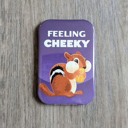 A two inch by three inch rectangular magnet featuring an illustrated chipmunk holding a peanut, set against a purple background. The text above the chipmunk reads "Feeling Cheeky."