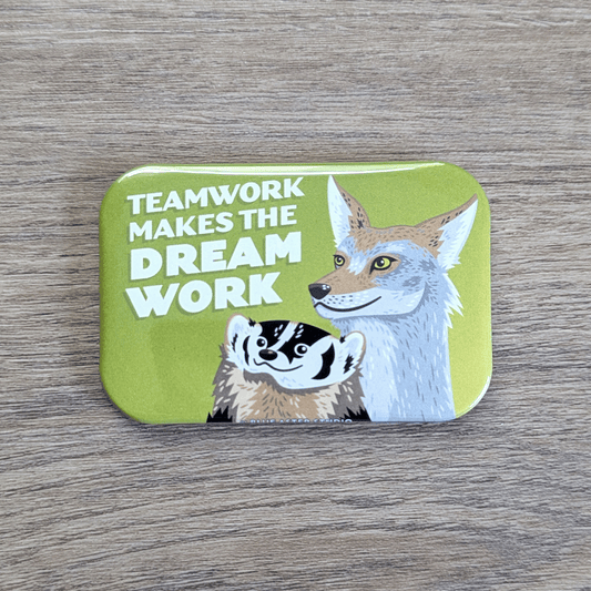 A rounded rectangle magnet featuring an illustration of a smiling badger and coyote gazing upwards at the text Teamwork makes the Dream Work.