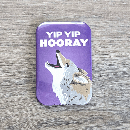 A rounded rectangle magnet of a coyote happily calling to the sky, with the text Yip Yip Hooray above it.
