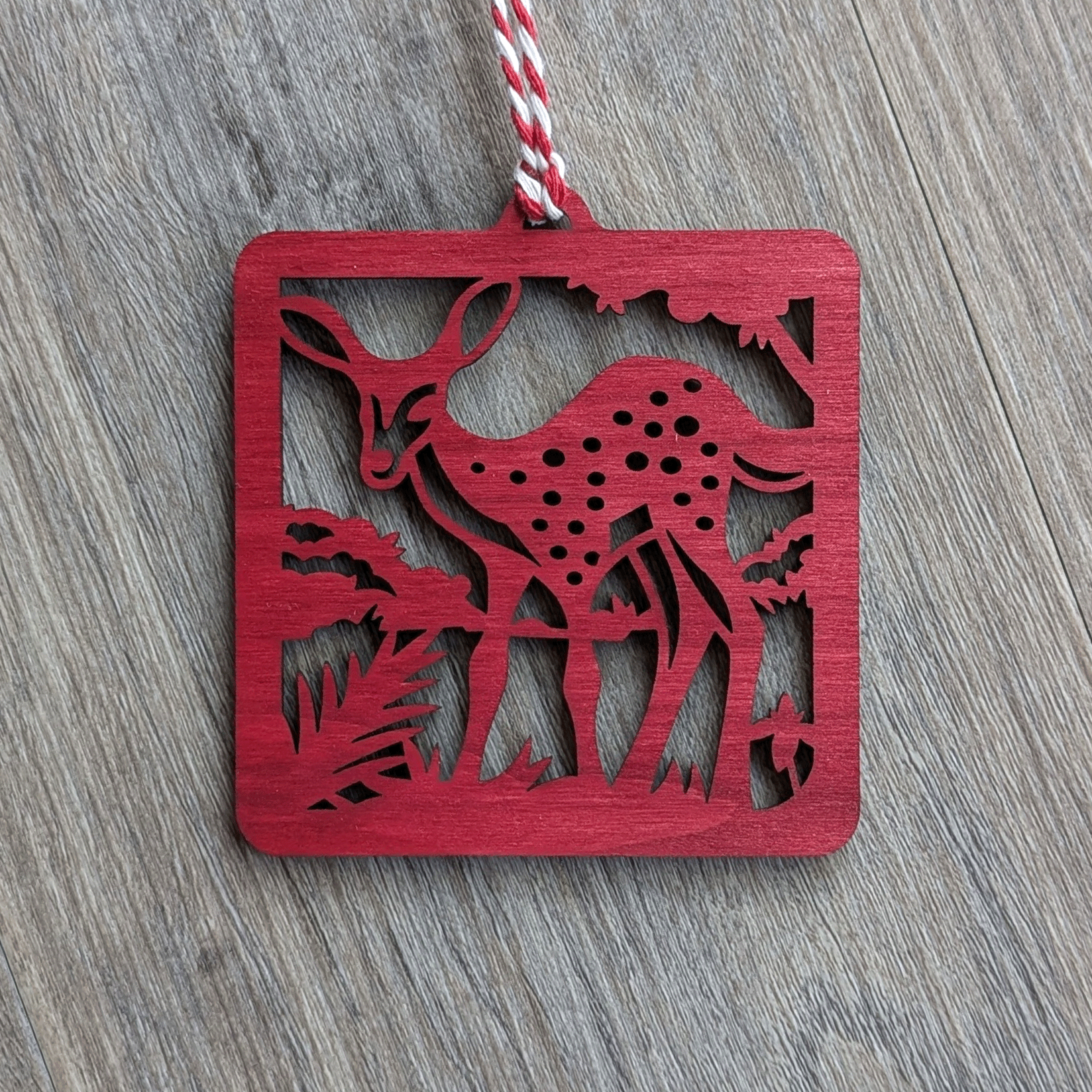 A square red wooden ornament of a spotted fawn.