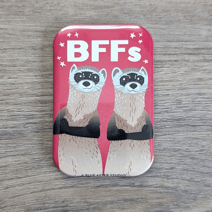 A rounded rectangle magnet featuring an illustration of two black-footed ferrets standing back to back and smiling with the text BFFs above them.