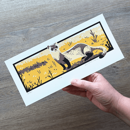 The black-footed ferret artwork being held in a hand to show the 4.5 inch x 10 inch scale.