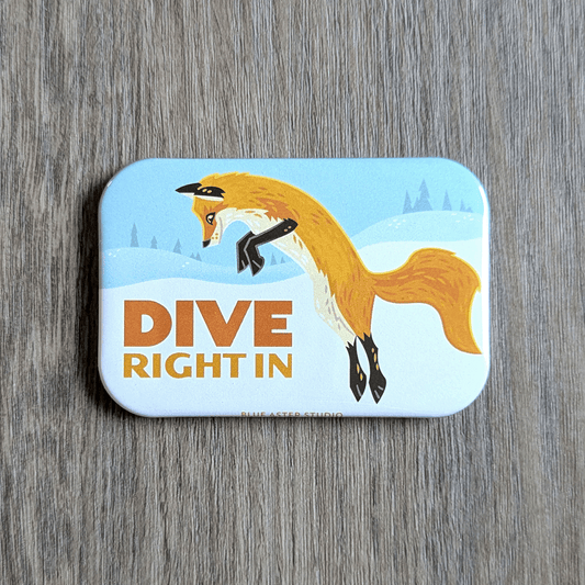 A rectangular magnet with an illustration of a red fox diving into the snow with the text dive right in