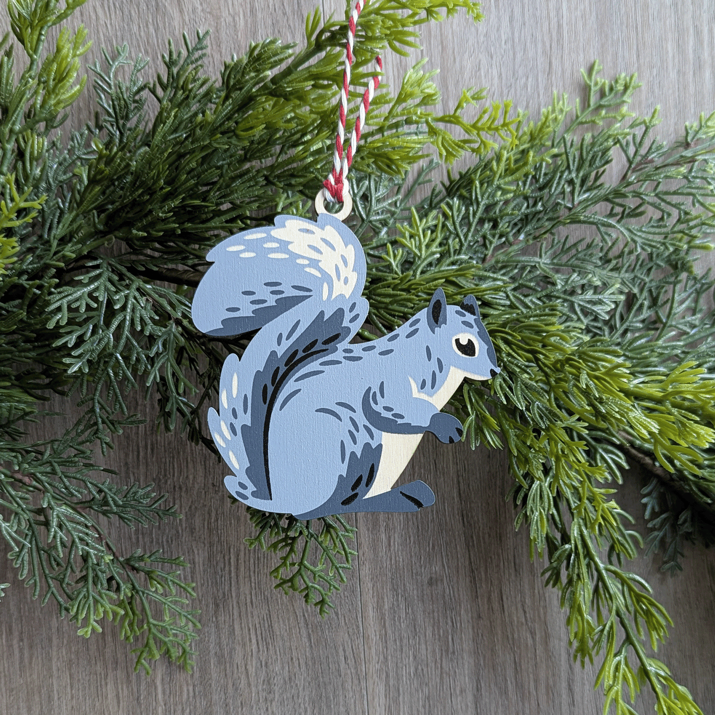 A wooden screen printed ornament of a gray squirrel hanging on a green garland.