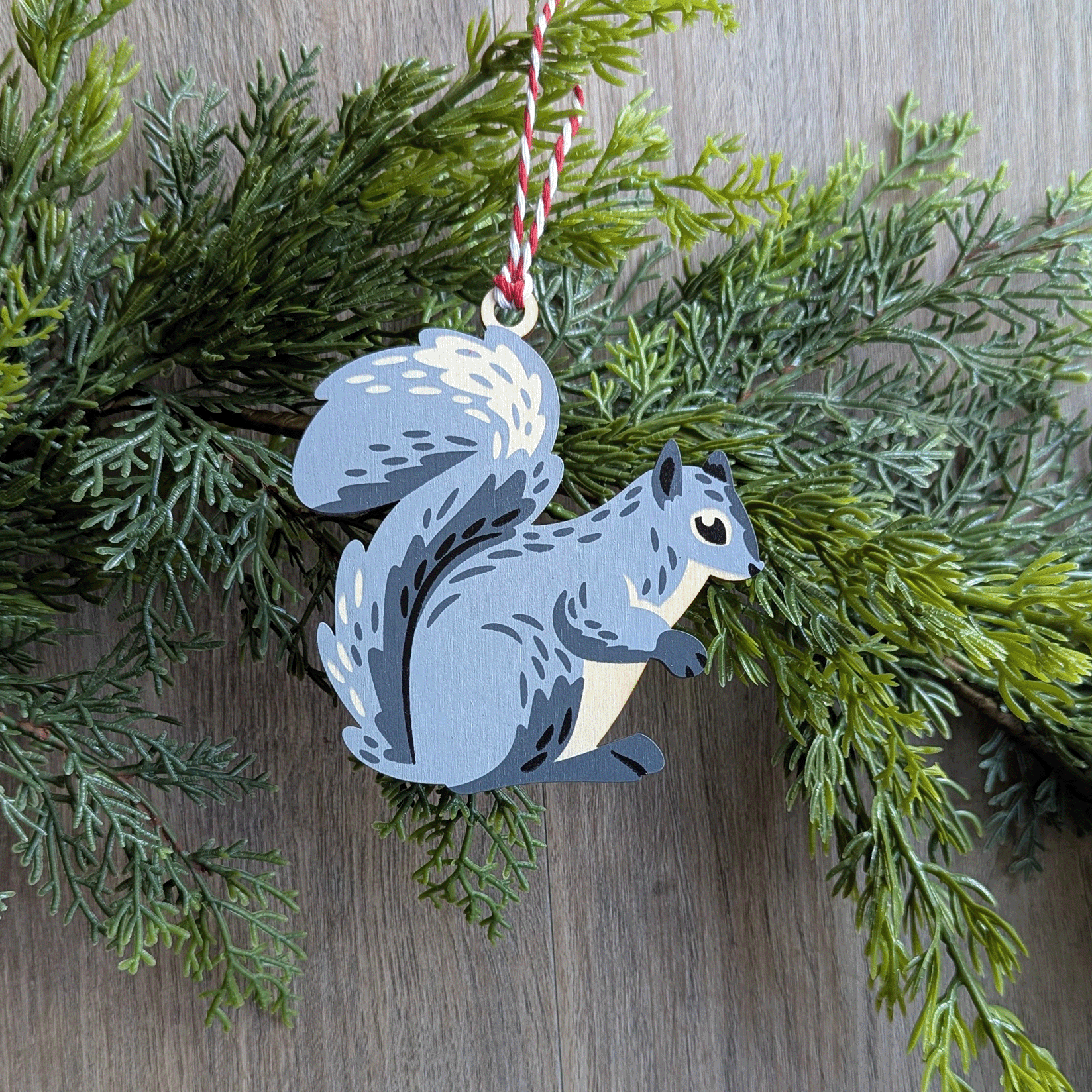 A wooden screen printed ornament of a gray squirrel hanging on a green garland.