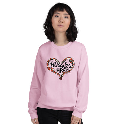 A female model wearing a pink sweatshirt with a pair of illustrated corn snakes forming a heart around the text "Hugs and Hisses"