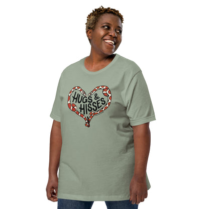 A female model wearing a sage green t-shirt with a pair of illustrated corn snakes forming a heart around the text "Hugs and Hisses"