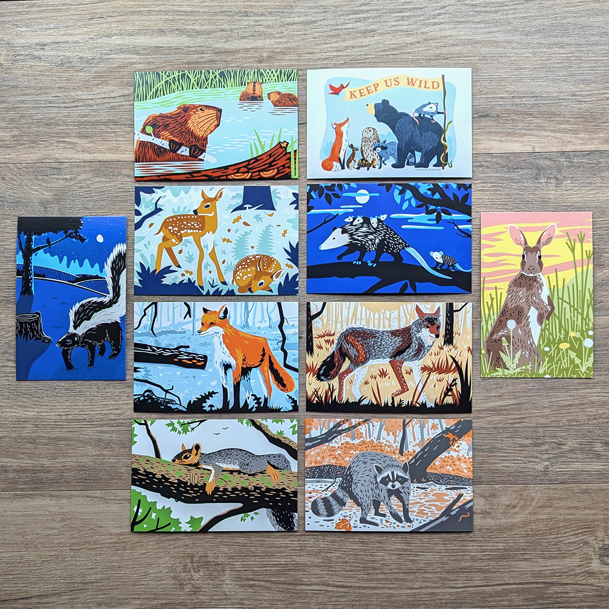 A selection of 4 inch by 6 inch postcards featuring colorful illustrations of wildlife including a beaver family, striped skunk, a pair of fawns, a red fox, a fox squirrel, a raccoon, a coyote, a rabbit, an opossum family, and a Keep Us Wild design with several animals.