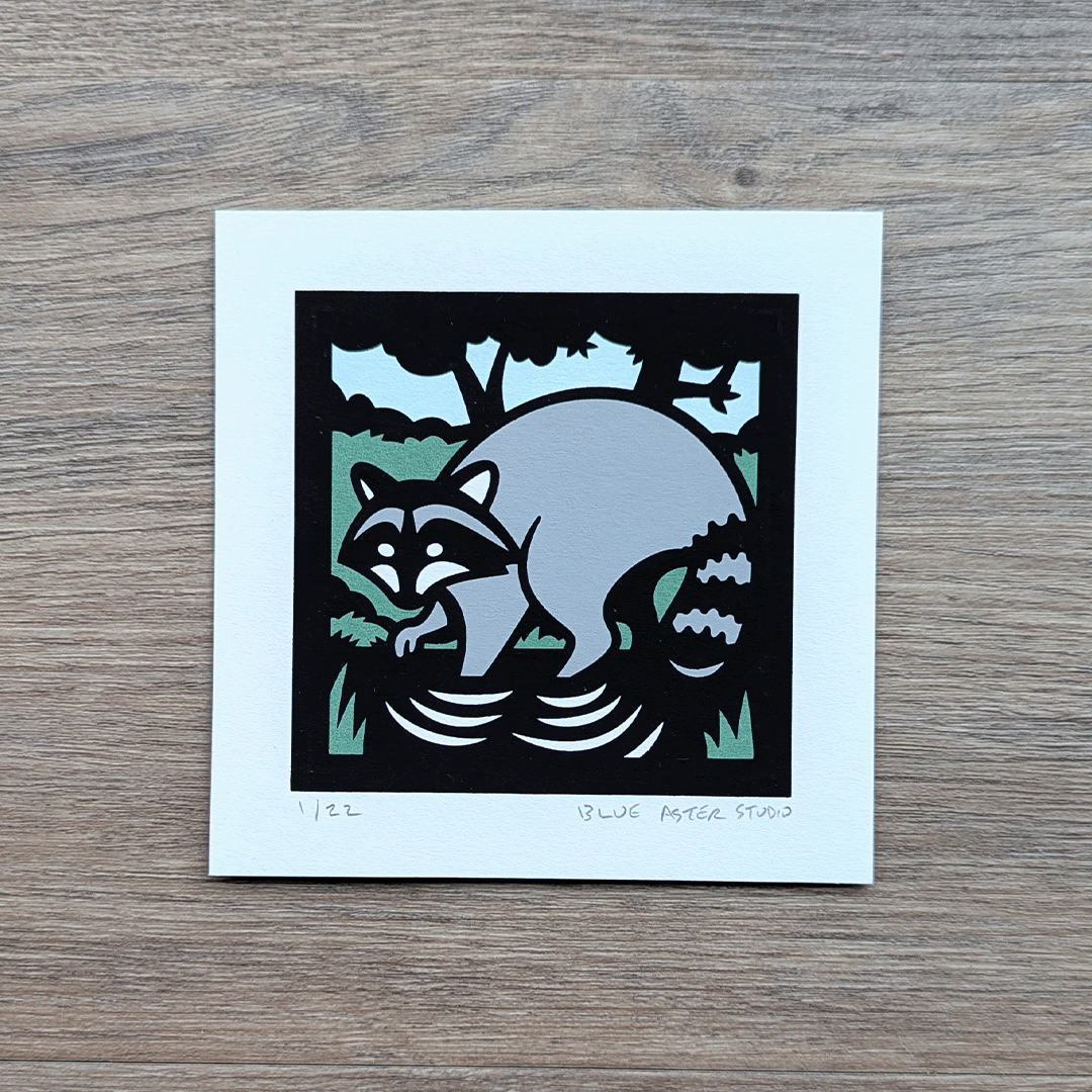 A 4x4 inch screen print of a raccoon printed in green, blue, gray, and black.