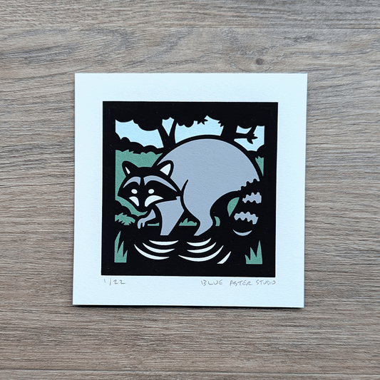 A 4x4 inch screen print of a raccoon printed in green, blue, gray, and black.