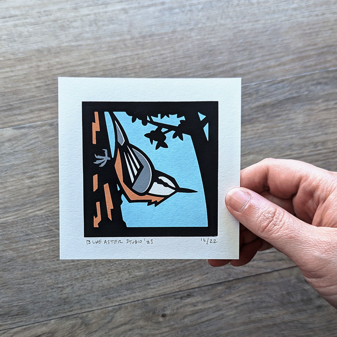 Hand holding a mini screen print of a red-breasted nuthatch.
